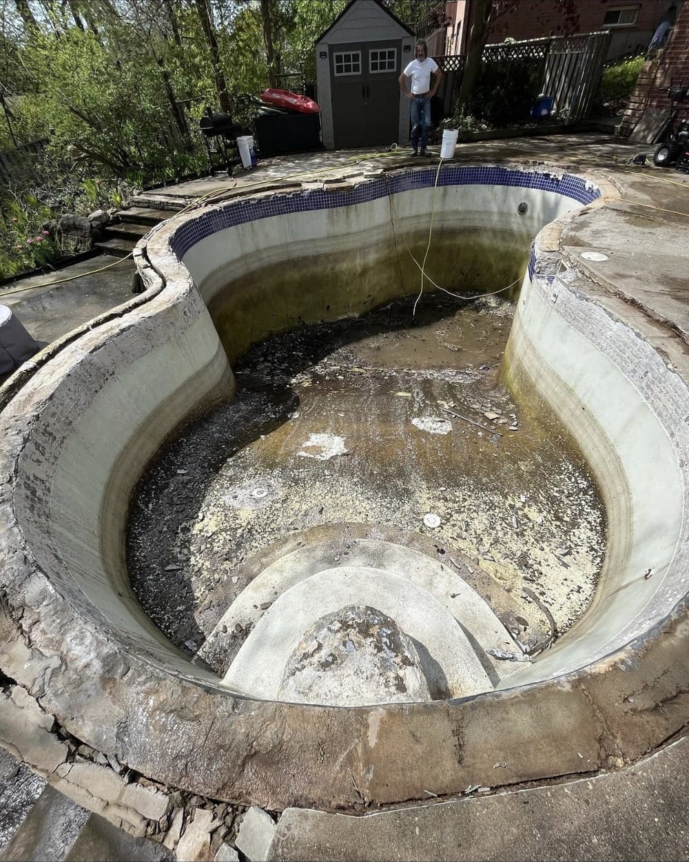 Drained freeform pool with a failing surface and debris, before renovation