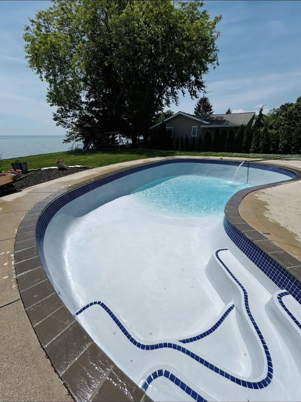 Same kidney-shaped pool after new white marbelite, blue waterline tile, step tile and coping