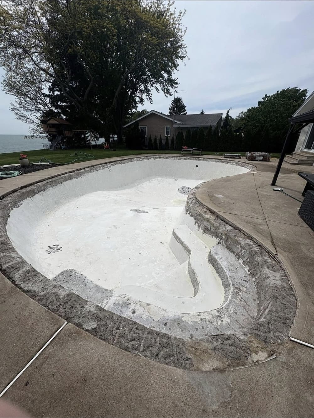 Kidney-shaped concrete pool with a worn white finish and coping removed, before resurfacing